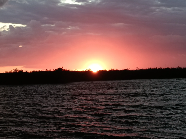 A sunset over the water with some clouds in the sky.