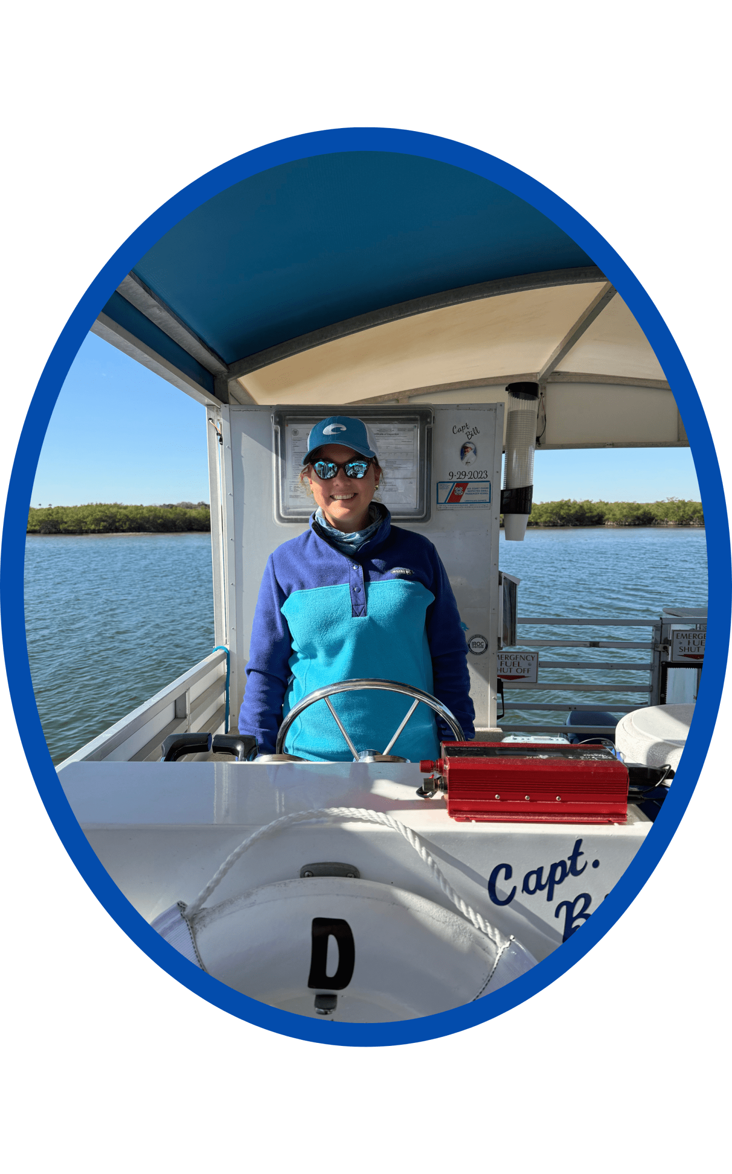 Person in blue jacket and cap steering a boat on a sunny day.
